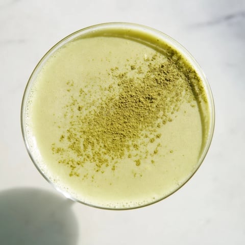 A chilled martini glass holds a creamy, pale green Matcha Martini Cocktail, garnished with a light dusting of matcha powder.