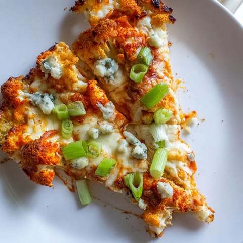Close-up of Buffalo Cauliflower Pizza with a bubbly cheese crust, fresh celery slices, and a tangy blue cheese garnish on a rustic board.