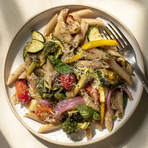 A close-up of steamy Pasta Primavera in a skillet, garnished with fresh basil and a squeeze of lemon, ready for a family-style dinner.  